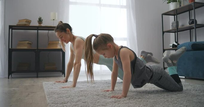 preschooler girl is training at home, mother is learning daughter to do push-ups, instilling good habits