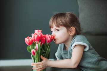 Beautiful little girl sniffing pink tulip