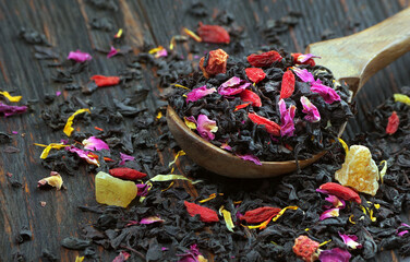 black blended tea with flower petals and dried fruit on a wooden spoon.