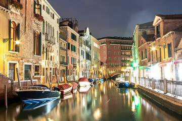 Fototapeta na wymiar Evening view of illuminated old architecture, floating boats and light reflections in canals water in Venice, Italy.