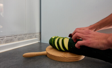 A wide-angle shot of a zucchini being cut a wooden cutting board in the kitchen