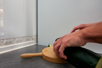 A wide-angle shot of a zucchini being cut a wooden cutting board in the kitchen