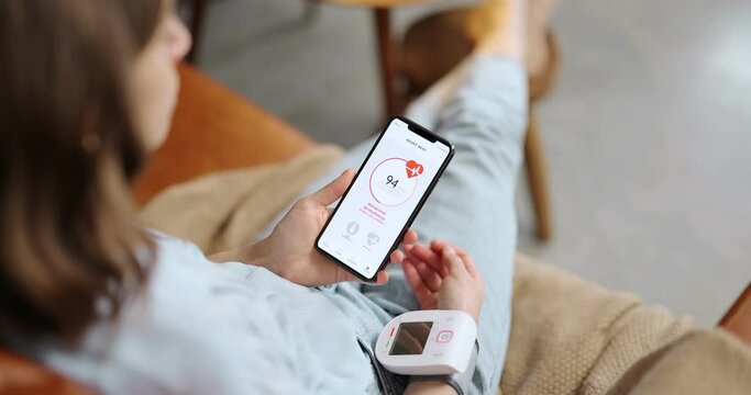 Woman measures heart beat, looking on a smart phone with running health program. Having arrhythmia and high heart rate. Modern gadgets for health monitoring