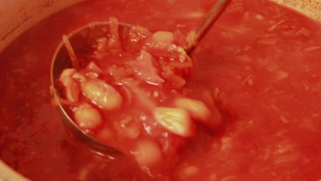 Traditional Ukrainian, Russian or Polish homemade borsch with meat and beans. Dish of national cuisine red soup in a saucepan cook interferes with a ladle