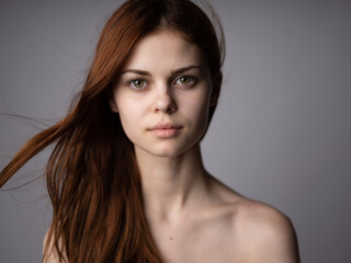 Fototapeta premium Portrait of a beautiful red-haired woman with bare shoulders on a gray background close-up