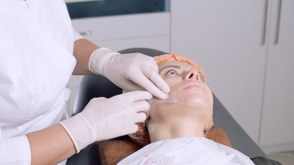 Obraz na płótnie Canvas Cosmetologist making treatment procedure to the patient. Beautician makes injections in the woman's face. Mesotherapy. Doctor in medical gloves put injections in female face.