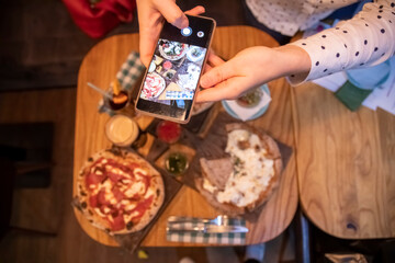 female hands takes pictures on a smartphone table with a delicious pizza in a restaurant