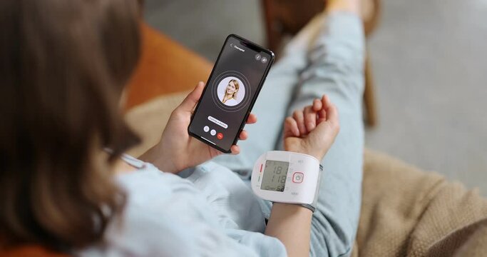 Woman measures blood pressure with wrist tonometer, calling a doctor with phone. onsultation with a therapist online and modern gadgets for health monitoring