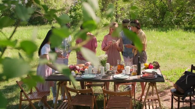 Slow motion wide shot of modern multi-ethnic friends standing at dining table getting ready for outdoor party