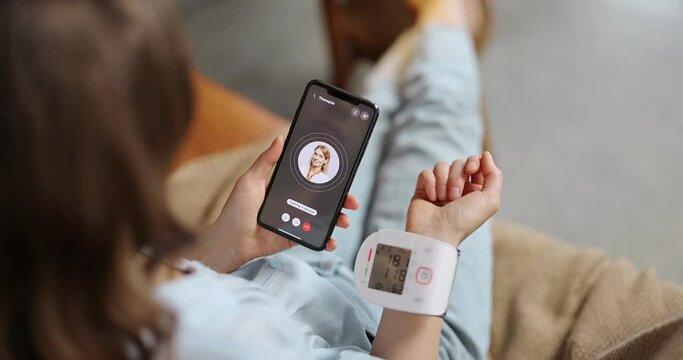 Woman measures blood pressure with wrist tonometer, calling a doctor with phone. onsultation with a therapist online and modern gadgets for health monitoring
