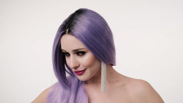 Portrait of Caucasian joyful stylish woman in lilac wig smiling to camera on light background. Close up of happy girl. Extraordinary female charm. doll look concept.