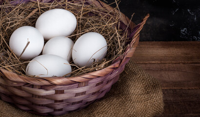 basket of white chicken eggs with hay on a rustic background, with a copy of the space
