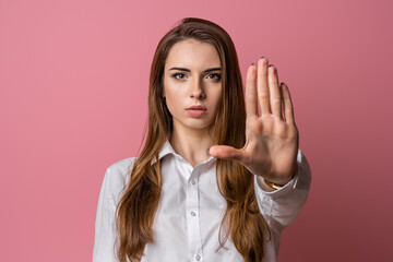 Serious brunette girl keeps palm forward at camera, makes forbid sign, restricts or warns, extends...