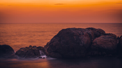 Colorful sunset and rock formation in foreground with waves crashing view from Galle Dutch fort evening, after sundown blue hour, long exposure photograph.