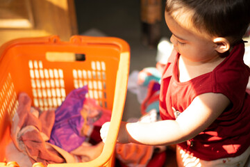 Asian Indian baby girl portrait closeup playing with Cloths bucket. A cute baby girl removing cloth from plastic basket