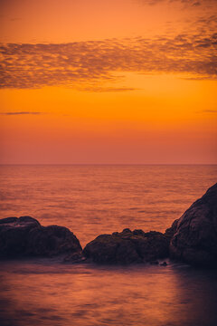 Colorful sunset and rock formation in the foreground with waves crashing view from Galle Dutch fort evening, after sundown blue hour, long exposure verticle landscape photograph.