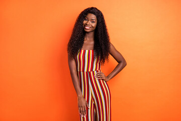 Photo of attractive pretty dark skin woman hold hand waist summer season smile isolated on orange color background