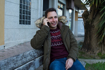 smiling man sitting on the bench using the phone