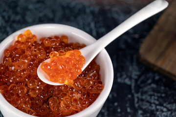 Close up delicious, crumbly, large red caviar in a white cup with a spoon on a black background.