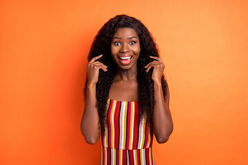 Photo of amazed shocked dark skin young woman hold hands hair good mood isolated on orange color background