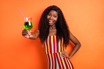 Photo of dark skin cheerful woman hold hand waist cocktail drink cheers isolated on orange color background