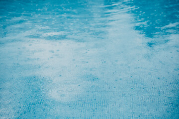 Rain drops falling on pool water, creating soft ripples.