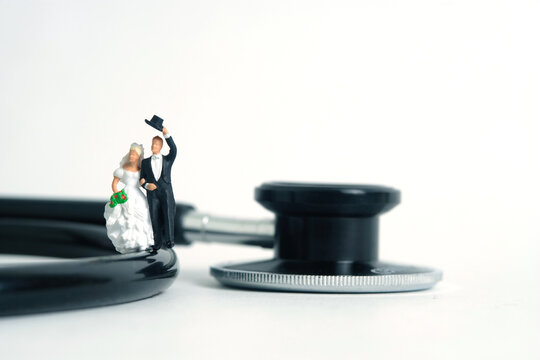 Wedding marriage and couple medical check-up concept miniature people toy photography. Bride and groom with stethoscope isolated on white background.