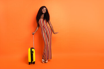 Full size photo of afro american young woman look empty space luggage trip isolated on orange color background