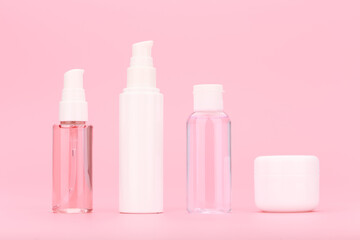Minimalistic still life with set of unbranded cosmetic bottles with cleansing gel, face cream, lotion and under eye cream against bright pink background. Concept of daily skin treatment