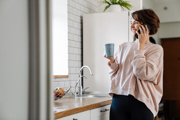 Joyful beautiful girl talking on cellphone while drinking coffee