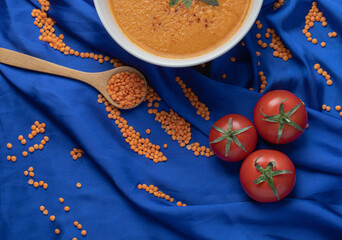 A white bowl of lentil soup with uncooked lentil beans and tomatoes
