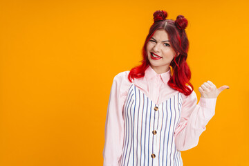 Beautiful girl with red hair winking while pointing finger aside