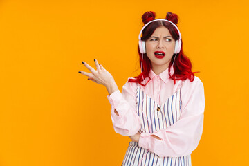Perplexed girl with red hair gesturing while listening music with headphones