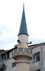 Obraz premium Minaret of a Muslim mosque in downtown Istanbul, Turkey on the background of the cloudy sky. Minaret with four speakers, invites believers to prayer. Tower at the mosque aspiring to heaven. 
