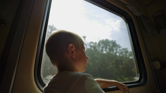 Kid looks out the train window. Thoughtful boy in a train compartment.  Boy is traveling by train. The child dreams of a fun summer vacation. Long-distance family trip. End of lockdown.