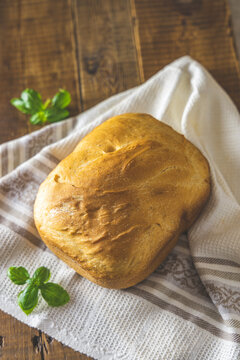 Loaf of freshly baked bread with basil on linen towel over rustic wooden table background. Shallow depth of field.