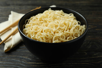 Napkin with chopsticks and bowl with noodles on wooden background