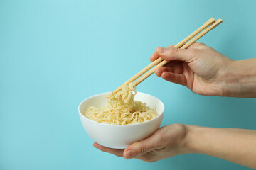 Female hands hold bowl with cooked noodles and chopsticks on blue background