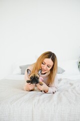 Cheerful young woman holding her big puppy with black nose and laughing. Indoor portrait of smiling girl posing with french bulldog