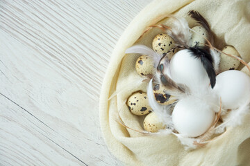 chicken and quail eggs with feathers in a towel on a dry wooden background simply
