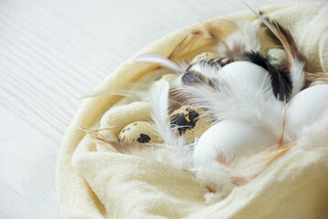 chicken and quail eggs with feathers in a towel on a dry wooden background simply
