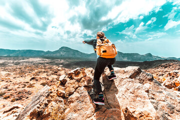 Woman with backpack hiking the mountains - Successful hiker on the top of the cliff pointing the sky - Sport, people and lifestyle concept