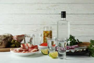 Shots of vodka and tasty snacks on white wooden background