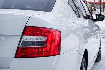Fototapeta premium In the foreground is the taillight and part of the trunk of a white car