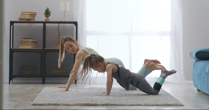 sporty family of adult woman and little daughter are training at home, doing push up on carpet in living room