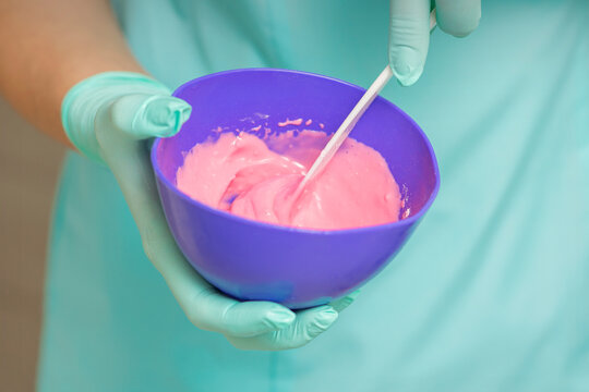 Close up of beautician's hands prepares pink alginate mask mixing in the blue bowl