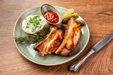 Fried pork ribs, pickles, potatoes and sauce on a blue plate