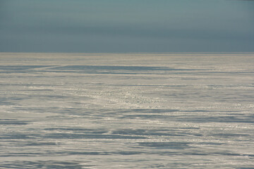 The icy desert that the winter-frozen Gulf of Finland has become, under the sky in a cloudy haze in direct sunlight.
