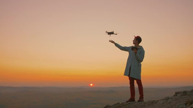 Man standing on top of mountain, starts drone from his hand, aircraft takes off