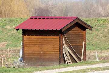 Back view of small garden storage tool shed made of wooden boards and metal roof tiles built in local urban garden on warm sunny winter day